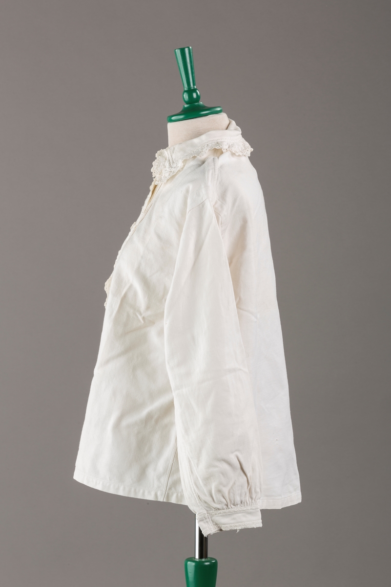 Form: Hoftelang trøye, Lange ermer, krage. Kragen og åpningen foran er kantet med  maskinprodusert blonde. Tre biser på hver side av åpn. foran. Lukkes med to løse knapper.