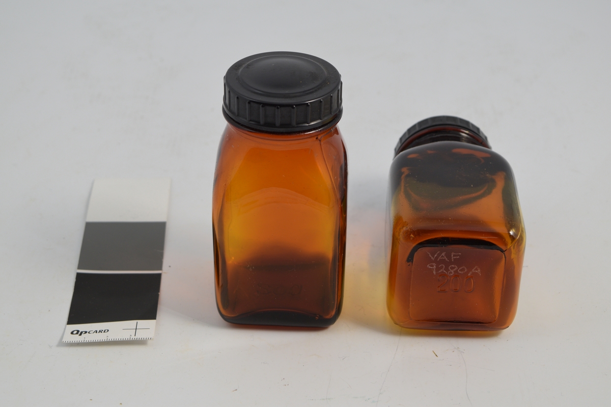 2 stk. brune, transparente, firkantede glasskrukker med sort rundt bakelitt lokk. Brukt til oppbevaring av tabletter i apotek og for salg.