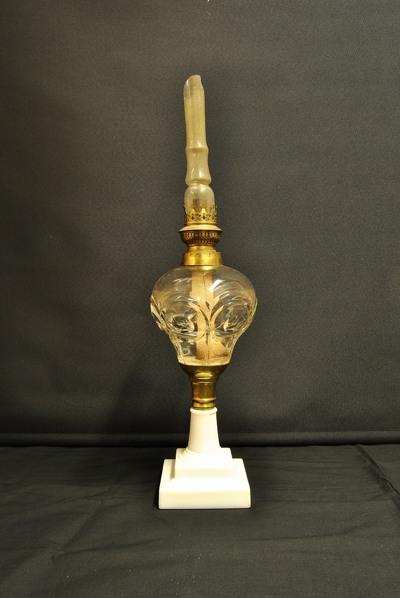 Form: Høg parafinlampe med glas behaldar for parafin og kvadratisk porselenssokkel. Laus kuppel.