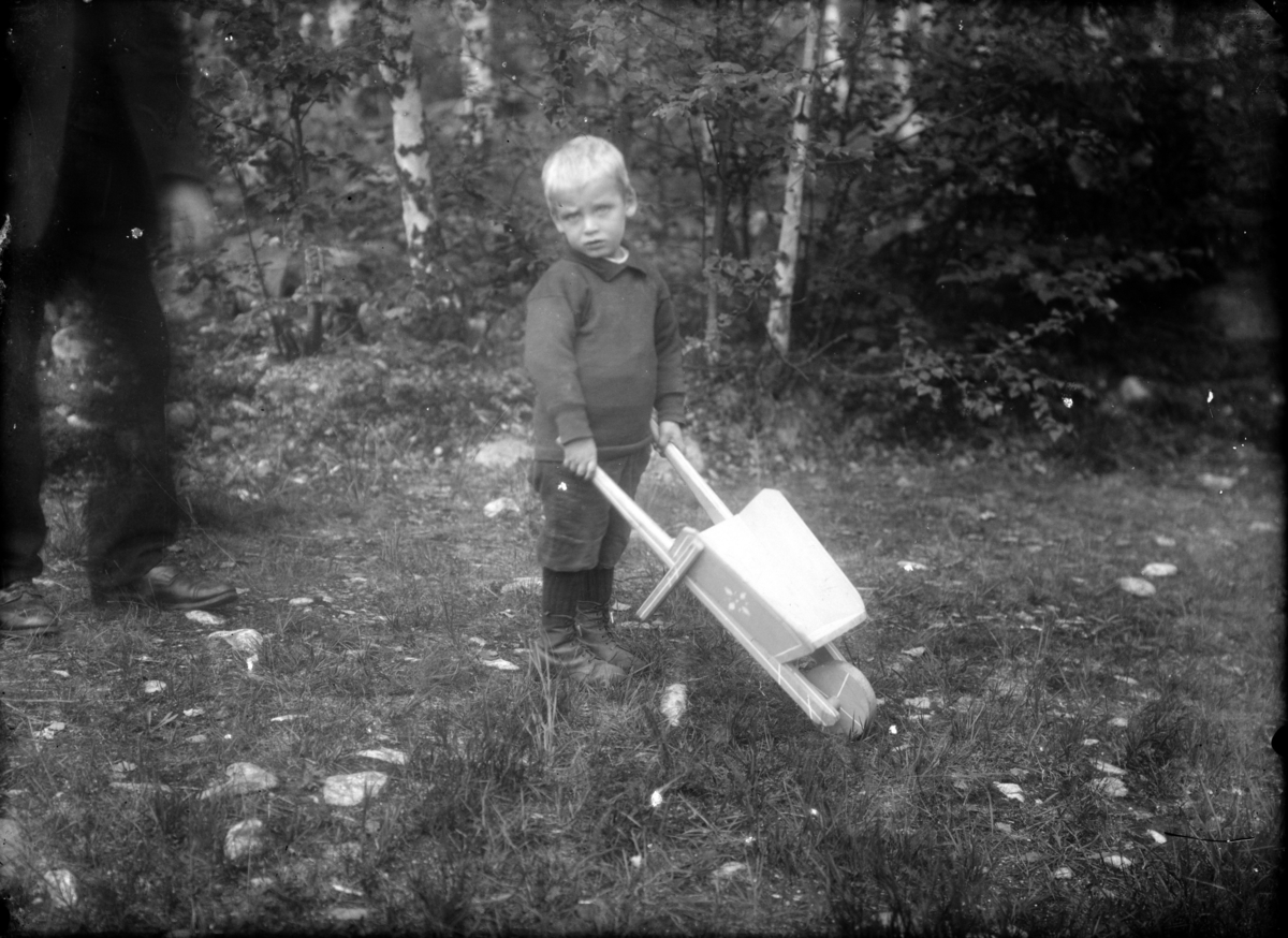 Gutt, liten (3-4 år) med liten trillebår i skogen, antakelig på Bådstø, Tretten