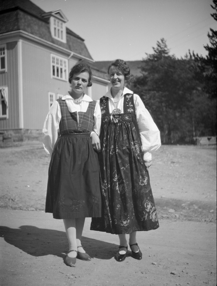 To kvinner  i bunader på Kommuneplassen, Vålebru. Fru Aaløkken til venstre med rondastakk og frk. Larsen med Hallingbunad.