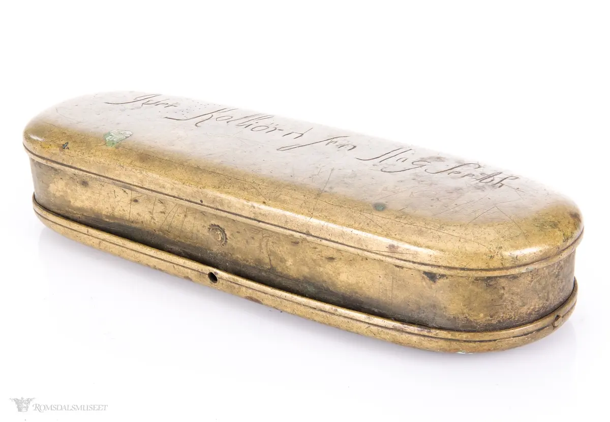 Rektangulær messingeske med avrundede ender. Har en påsatt og påklinket utenpåliggende bunn og utenpåliggende, hengslet lokk