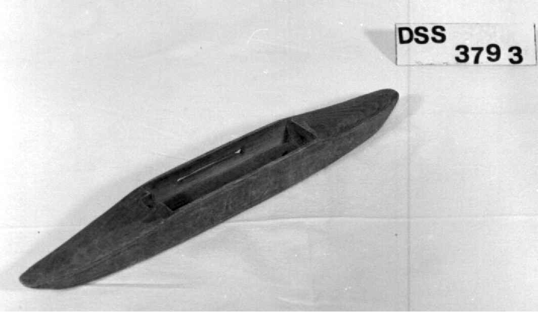 Avlang vevskyttel av tre med uthuling på midten, der hullet i bunnen er formet som en ranke.