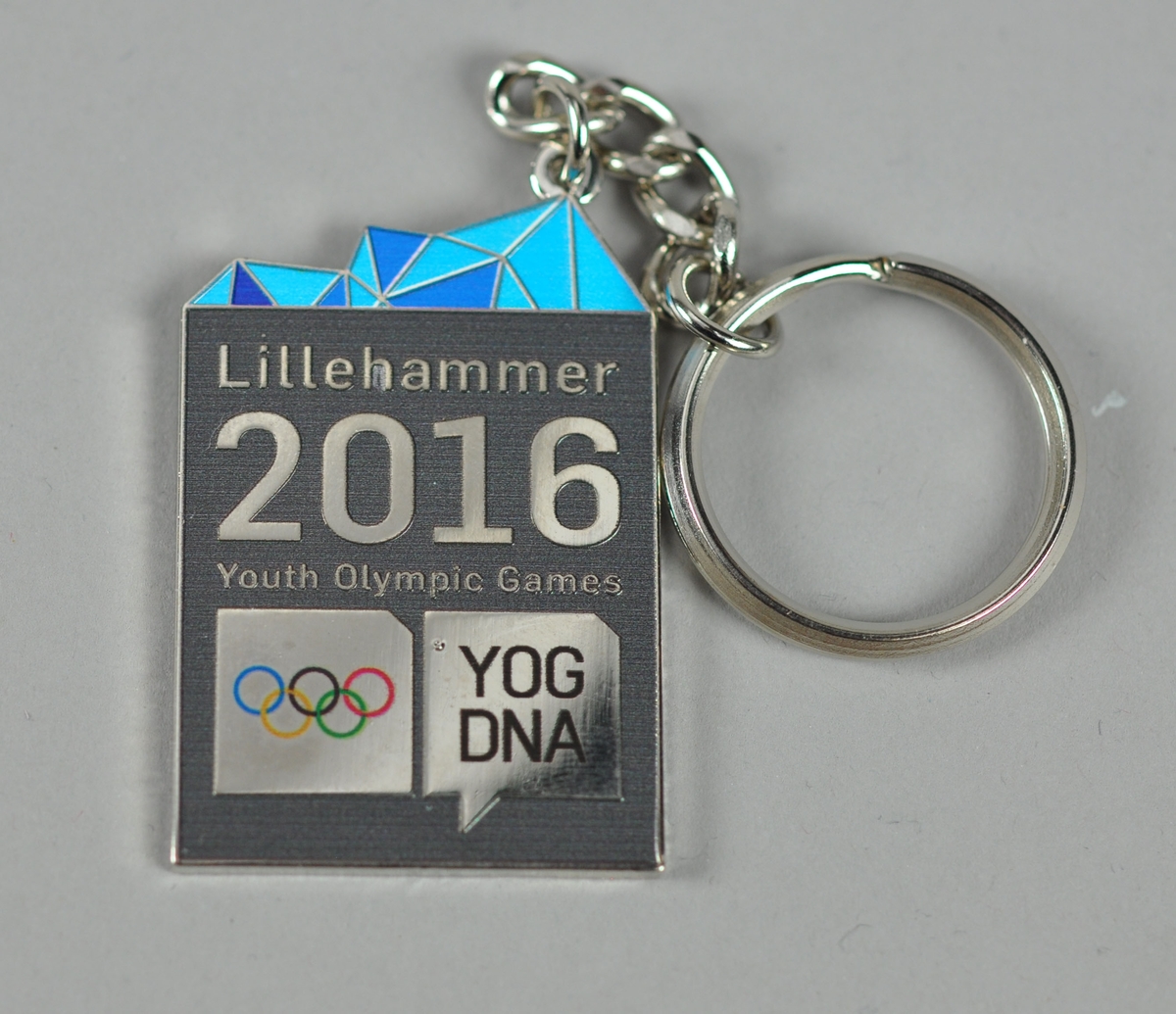 Nøkkelring i metall med tekst og logo for Lillehammer Youth Olympic Games 2016. Dekor ihht designprogram på toppen.
