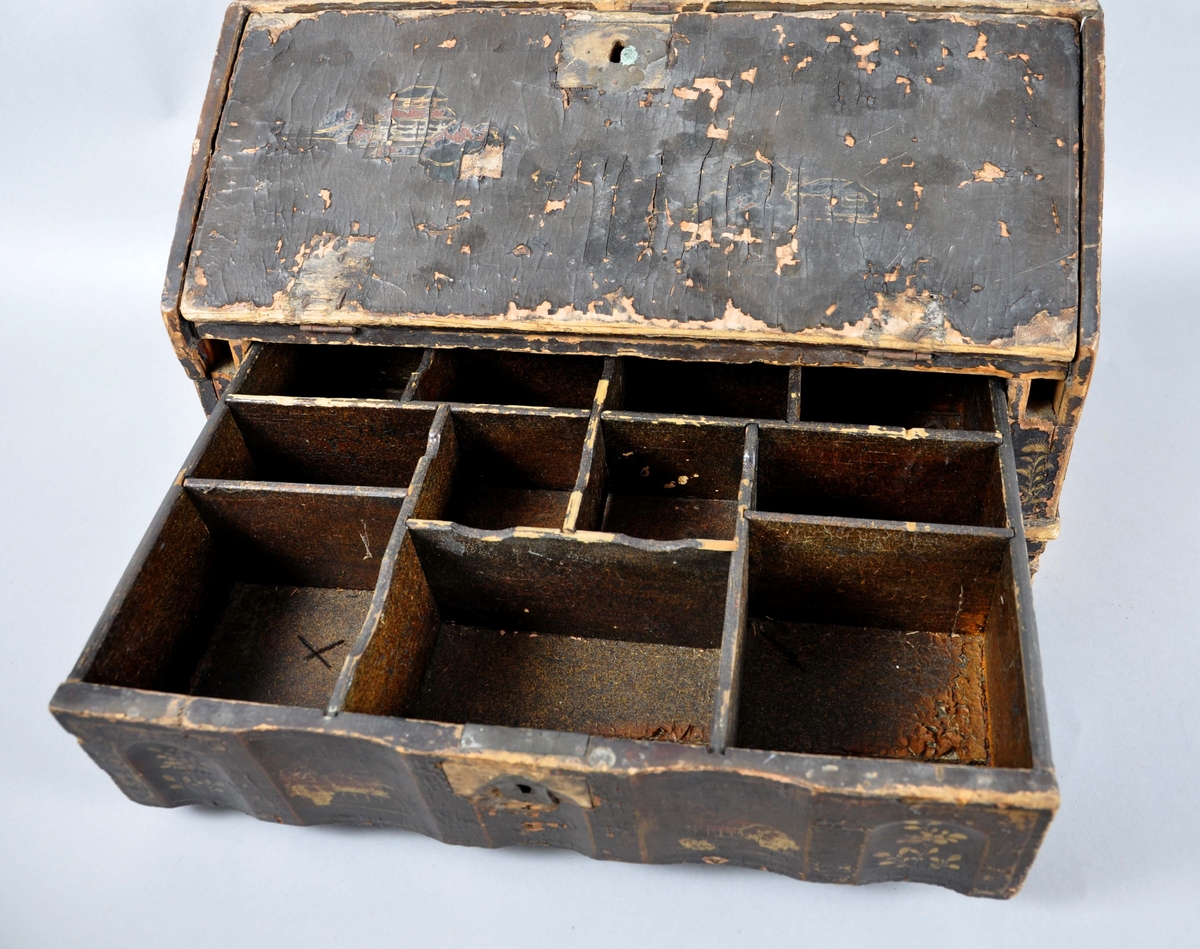 Reiseskrin av tre, rektangulær form med skrå framside. Skrinet har brun grunnmaling og gullfarget dekormaling oppå. Malingen har i stor grad falmet av og bare litt av dekormalingen er synlig. På framsiden av skrinet, nederste del, er det en skuffe med seksjonerte avdelinger. På øverste del er en nedleggbar plate med skuffer på innsiden. Staver som kan skyves ut og støtte platen mangler. På innsiden av platen er grunn- og dekormalingen bedre bevart. På sidene av skrinet er det hengslede hanker. Skuffe og plate har nøkkelhull, men nøkkel mangler.