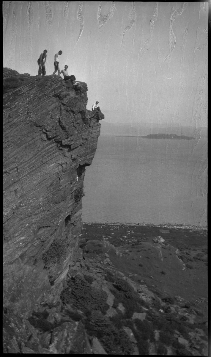 Harald Bergsaker, Ottar Roaldsøy, L. Fosse og Lindtner på den søndre enden av øya Hidle, øst for Stavanger. De er på kanten av et stup og hviler i gresset under stupet. En av dem ser utover sjøen med kikkert. Seilbåten "Vilja ligger i bakgrunnen.