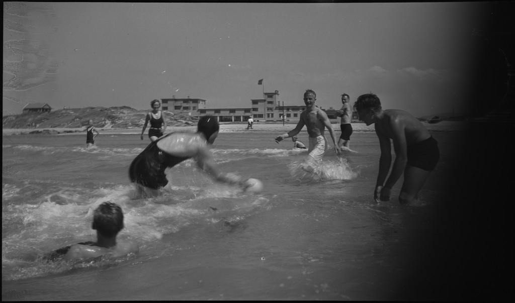 En stor vennegjeng i lystig lag på stranda på Sola. De har trommer og trekkspill og leker i vannet og på land med og uten ball. Sola strandhotell ligger i bakgrunnen. Tor Johannessen og Harald Bergsaker er på bilde nr. 14 og 18.