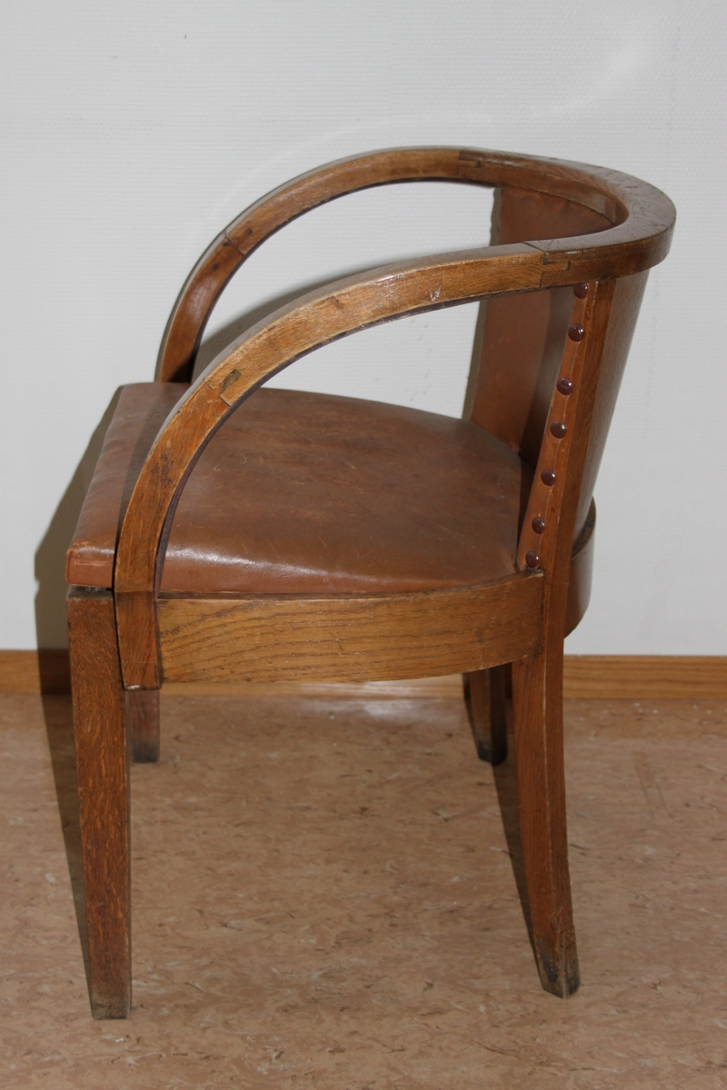 Møteromstol/kontorstol med armlener samt buet rygg. 4 ben. Metallbeslag under armlener. Brunt skinn i rygg og sete. Stolen er lakket med klar lakk. Originalt møbel innkjøpt til det nye Statsarkivet i Kristiansand i 1935.