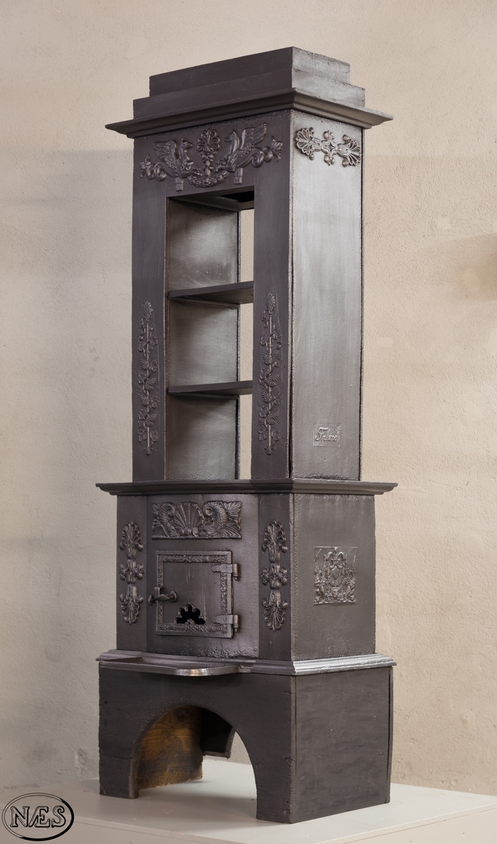 Ovnen består av to avdelinger. Underdelen har et frembuet midtparti med kamskjell flankert av sjødyr på hver side. På kortsidene skjold, løvehode og symmetriske ørner. På bakplate en krukke med symmetriske engler.
Overdelen er høy, firkantet med tredelt åpning. Empire ornamentikk og avtrappet topp. Øverst på frontplaten symetriske fabeldyr (pegasus) vendt mot hverandre.