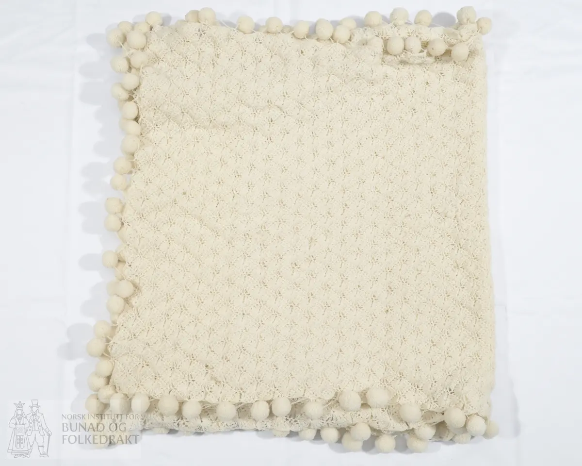 Skjerf. Heklet av tynt hvitt ullgarn. Med påsydde hvite pompomer hele veien rundt, også på kortsidene.