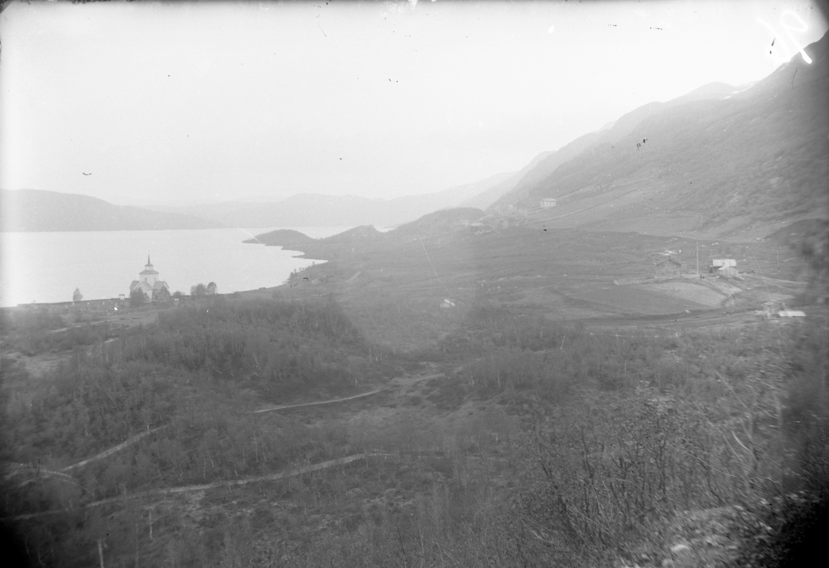 Rikard Berges fotoarkiv. Landskapbilde. Raulan kirke til venstre i bildet, og til høyre Rauland prestegård. I bakgrunnen Nigard. Bilde er tatt i 1904.