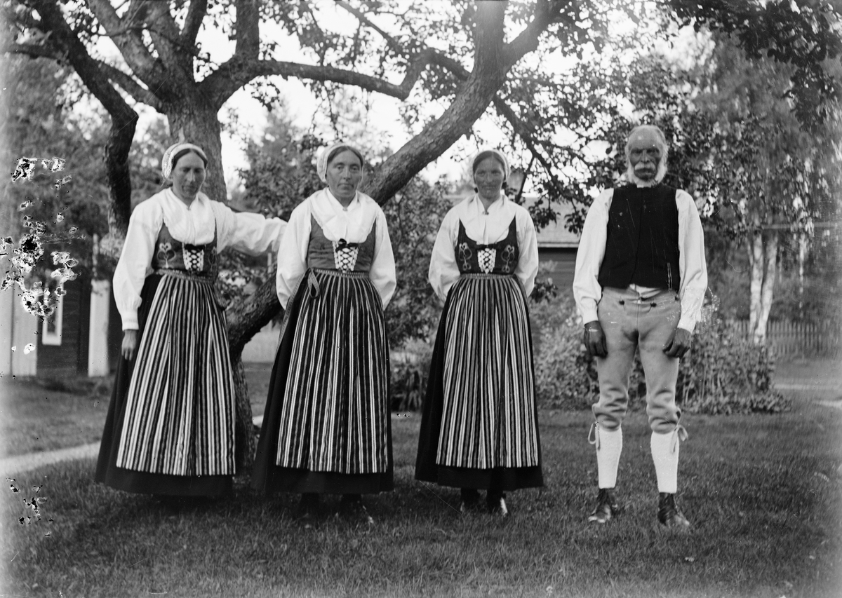 Svens Olle med sina tre döttrar Kristina, Anna och Britta, klädda i folkdräkt, står i trädgården på Svensgården, Dalarna, Sverige 1919