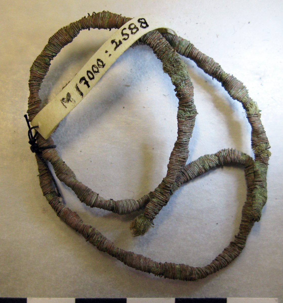 Metalltråd gjord av platt metall (lan), troligen av brons, lindad runt en växtfiberkärna. Tråden är "vriden" på längden troligen på grund av hur den använts. I ena änden är den avslutad och i den andra trasig/avsliten. Metalltråden kan ha använts som en s k galon, ett dekorband av metalltråd som sys på ett klädesplagg el dyl. Se exempel på Gustav II Adolfs tröja från 1661 på bifogad bild under Referenser/länkade filer.