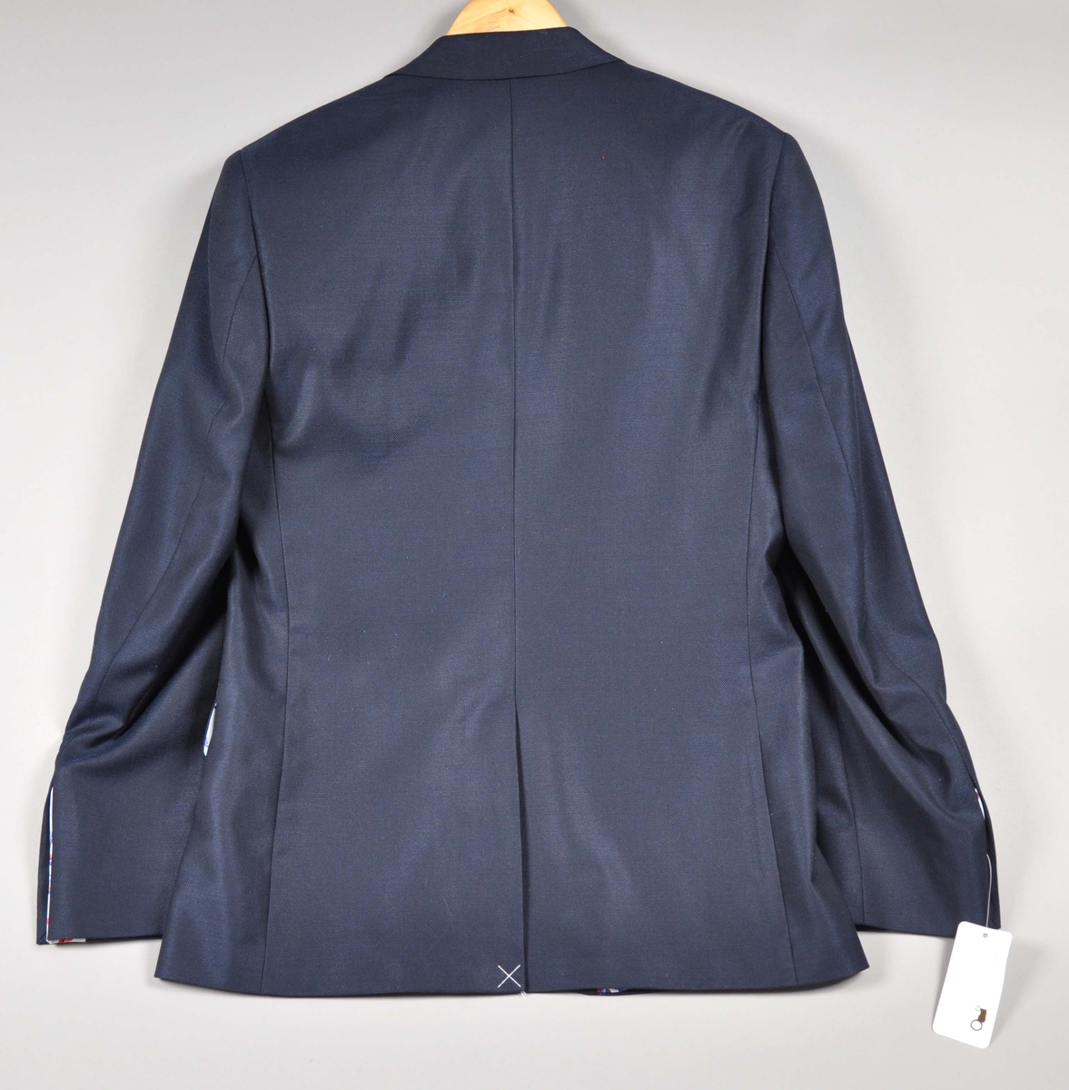 Mørkeblå dressjakke av ull/silke, foret med samme silkestoff som i damekjolen og tørkleet, et
hvitt silkestoff med "rosemalt" mønster.Jakken har fire innerlommer, en med knappelukking.
Utvendig to jakkelommer med klaff foret med silkestoffet, en brystlomme med påbrodert
"traktorlogo", Mørkeblått kantebånd fra kraven og ned. Lukket med en stor stoffknapp på ermene, fire ganger to mindre stoffknapper i hvitt (2), rødt og blått. På høyre erme brodert:Heia Norge i henholdsvis rødt og hvitt.
Str.:48