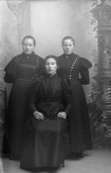 Gruppe, tre kvinner hvor ei sitter på stol, helfigur. Nevnt 