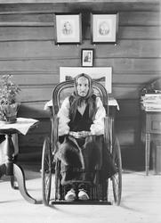 Eldre kvinne fra Otta i damaskstakk sittende i rullestol. Gu