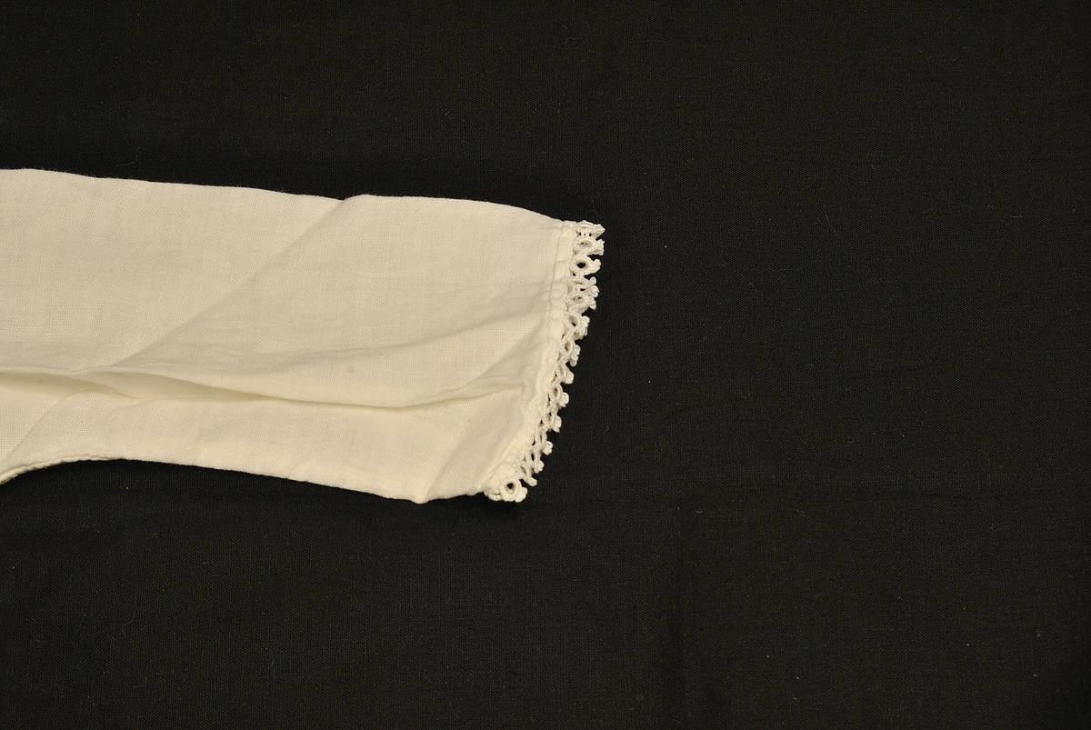 Rektangulær form. Knytinger bak. Nuppereller på krage og ermene.