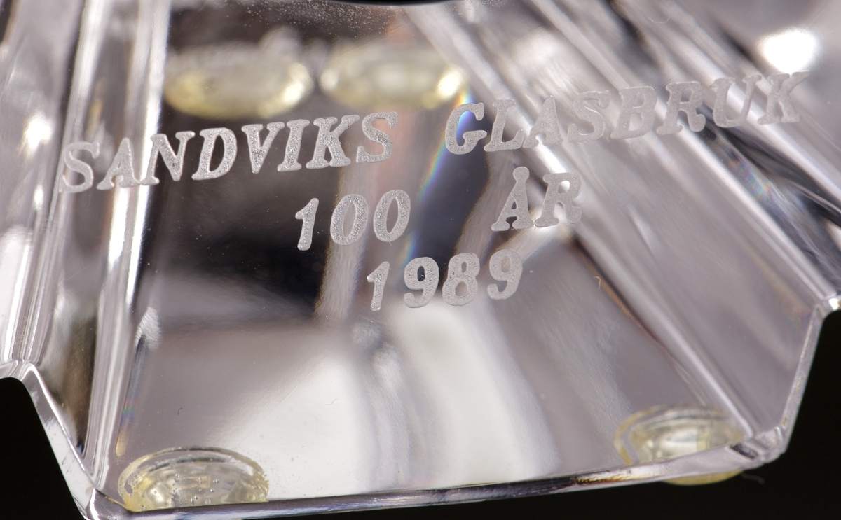 Klocka med fodral av glas. 
Urtavlan märkt "Orrefors".
Klockan togs fram till jubileumsåret 1989 då dotterbolaget Sandviks glasbruk fyllde 100 år. Klockor delades ut till personalen vid högtidhållandet av jubileet.
