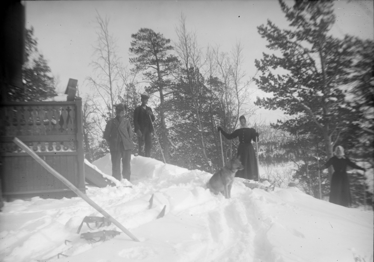 Eldre mann og hund ved hus sammen med en mann og to kvinner som står på ski