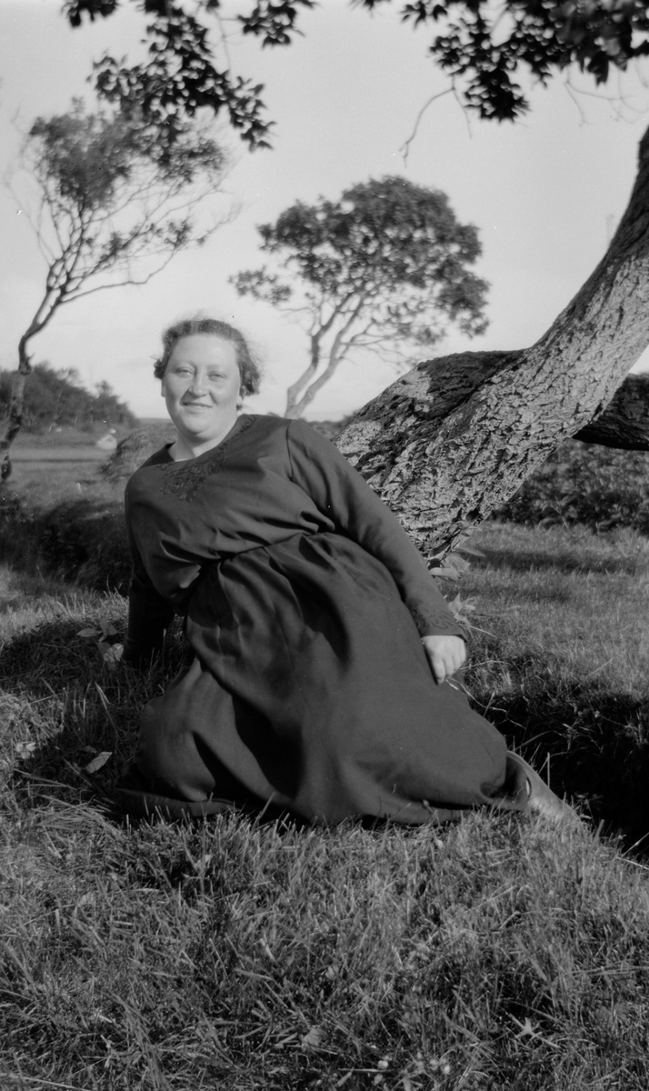 Kvinne sitter i gresset lent mot et tre