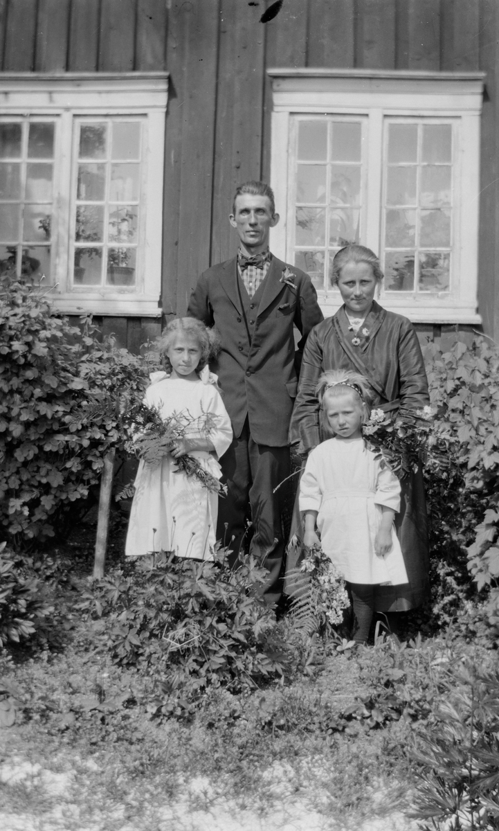 Kvinne, mann og to jenter foran hus.