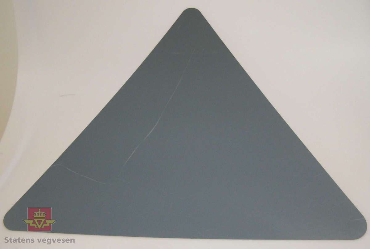Trekantet skilt av 3 mm plast, skiltet har avrundede hjørner. Rød bord og svart symbol på hvit lysreflekterende bunn. Symbolet varsler om innsnervring i kjørebanen, (smal veg). Grå bakside.