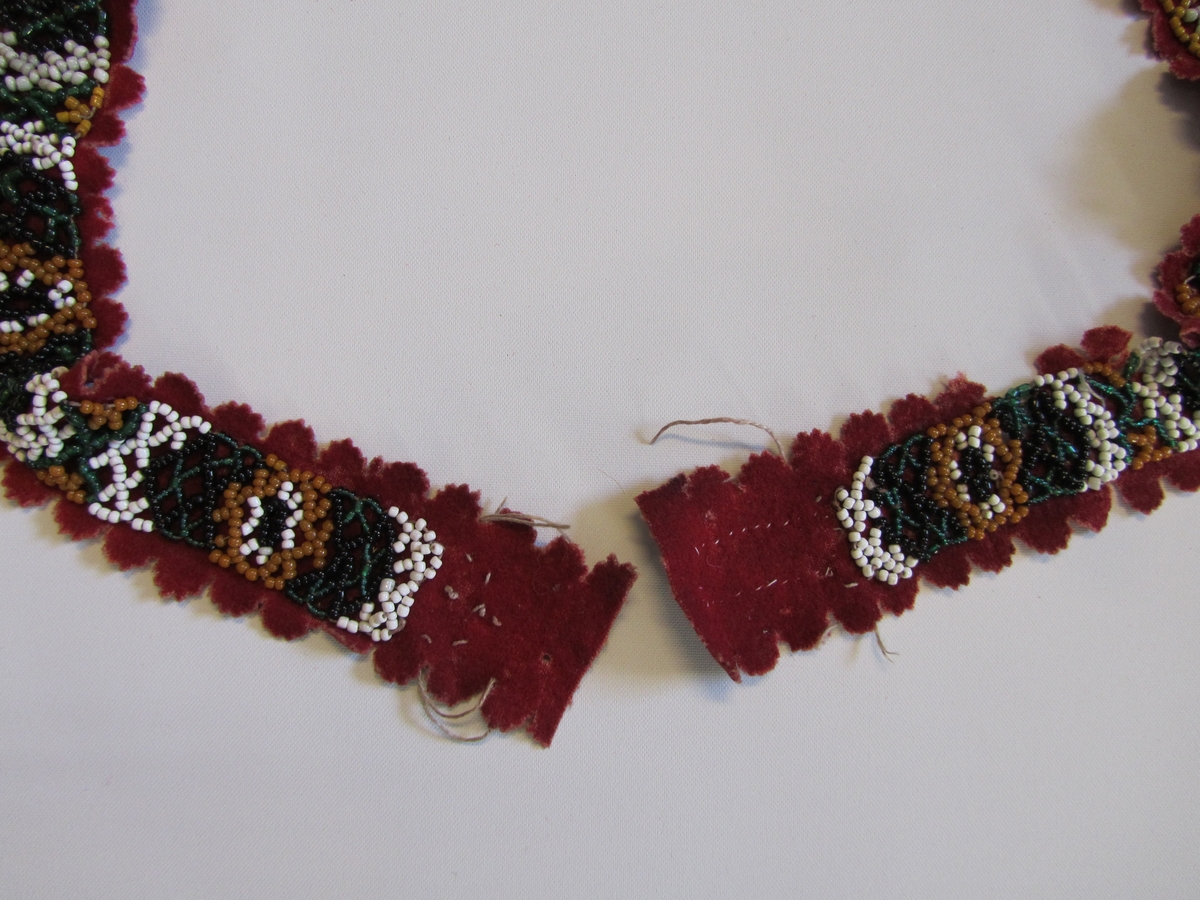 Belte med botn av rødt klede. Tredd band av småperler i forskjellige farger er påsydd. Langsidene og eine enden har utstansa, taggekant med halvsirkler  ca 1 cm i diameter. Manglar spenne.