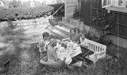 Kvinner og barn spiser et måltid i hagen utenfor enebolig på