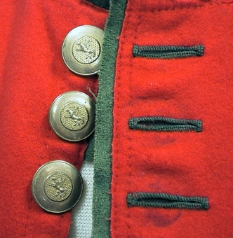 Mansväst av rött kläde med foder av linne. Framkanterna är kantade med grönt kläde samt 12 mässingknappar finns isydda på högra framstycket och 12 knapphål tränsade med grön lintråd på andra framstycket. Två stolpfickor är kantade med grönt kläde och med tre gröna tränsar vid var sida. Skört baktill i ryggen är bandkantat med grönt kläde. Prickstickningar runt alla kanter och på fickorna.