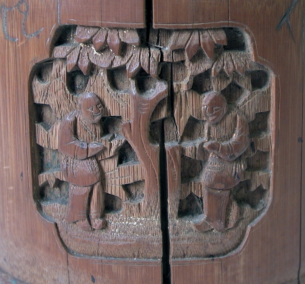 Burk av trä med fyra utskurna reliefer föreställande människo- och djurfigurer.