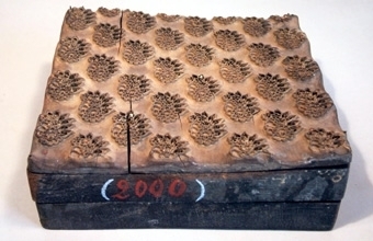 Tryckstock av trä med metallstift. Utskuret och stiftat mönster i form av blad och blommor i små grupper.
