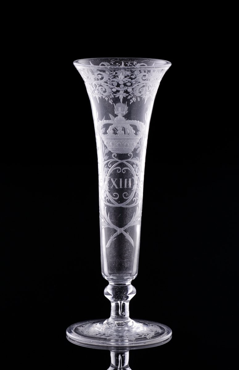 Champagneglas/strut på fot med omvikt kant.
Graverat spegelmonogram under kunglig krona: "C XIII"* med lagerkrans m.m.. 

* Carl XIII (1748-1818, reg. 1809-1818)