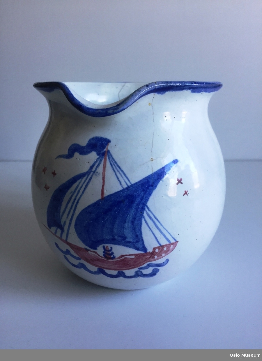 Keramikkmugge, glasert i hvit bunnfarge med seilbåtmotiv. Blå hank og kant .