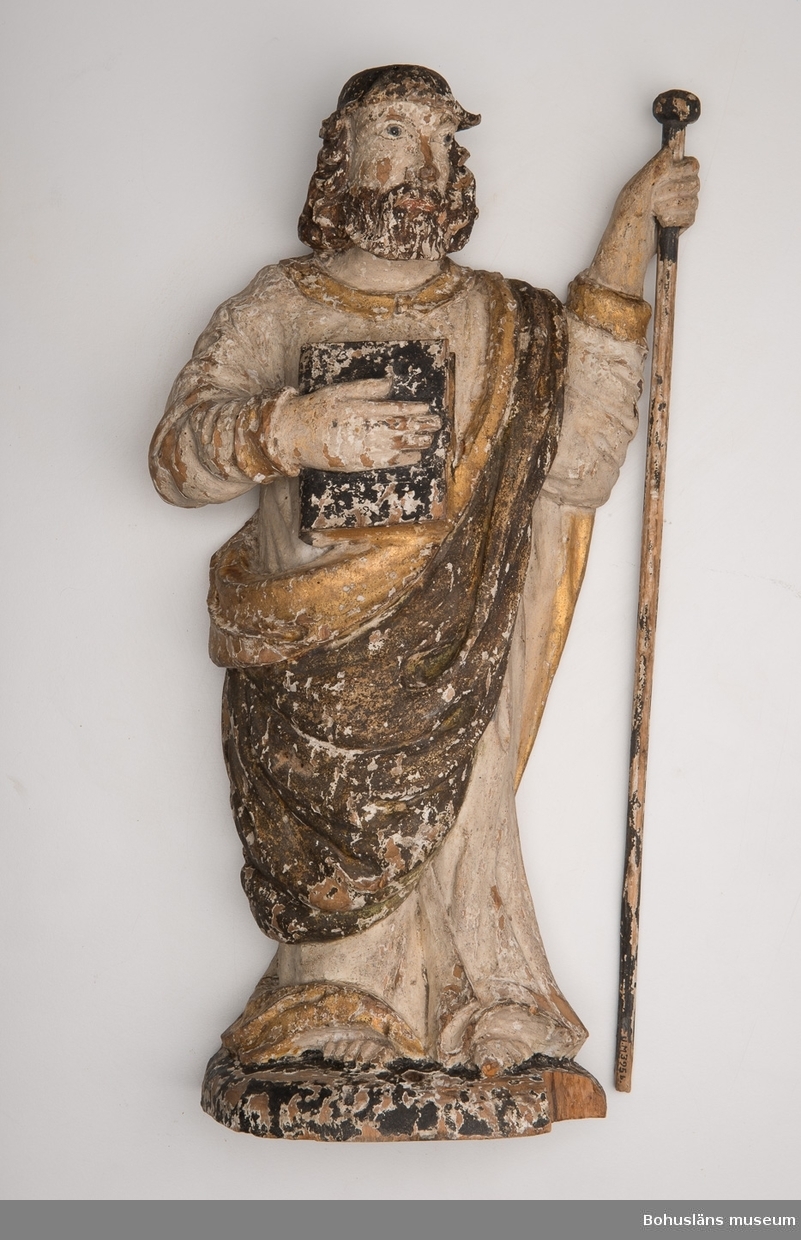Träskulptur, apostelbild från 1600-talet som tilhör altartavla UM000393.  Förgyllningen som uppvisar båda bladguld, slagmetall och/eller silver.
UM000395a = själva skulpturen,  UM000395b = skulpturens lösa stav.

Enligt katalogkort föreställer skulpturen helgonet och aposteln Jakob den äldre; tillhör altaruppsats UM000393a-i.
Vandringsstaven brukar attribueras till Jakob den äldre.
Krederat trä med mager oljefärg och oljeförgyllning. 

Ur handskrivna katalogen 1957-1958:
Apostelbild, Lane Ryr
H. 39 cm; höger hand håller en bok, vänster en stav b) L. 39,5 cm. Färgen delvis flagn.; små bitar avslag.

Lappkatalog: 13

Se foto på föremålet i Uddevalla museums kyrkliga utställning 1920, UMFA53292:0013

Ur Nationalencyklopedin, NE.se:  Apostel
I konsten framställs apostlarna alltid barfota samt klädda i tunika och mantel. De bär oftast en bok samt sitt individuella attribut, i allmänhet respektive martyrredskap (Petrus bär dock himmelrikets nycklar).
