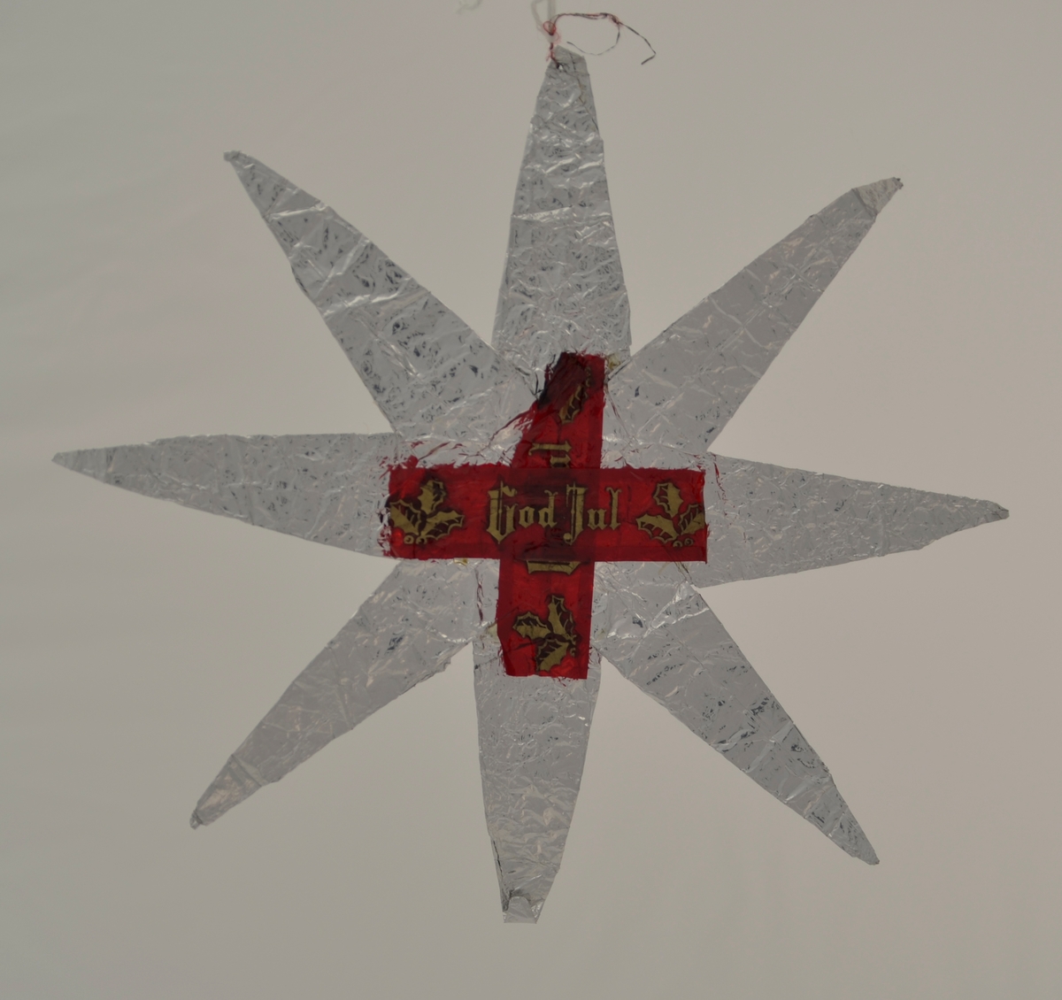 Form: 8-arma stjerne laga av sølvpapir, truleg sjokoladepapir. På kvar side av stjerna er det krosslagt, raudt cellofan med teksten "God Jul" - også dette truleg opphaveleg sjokoladepapir.