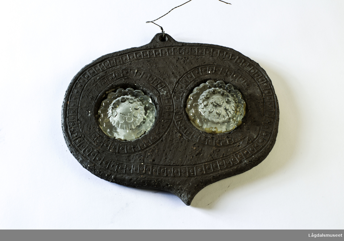 Skulptur formet som et uglehode. Selve hodet i keramikk utført av Rolf Hansen og øynene i glass utført av Benny Motzfeldt.