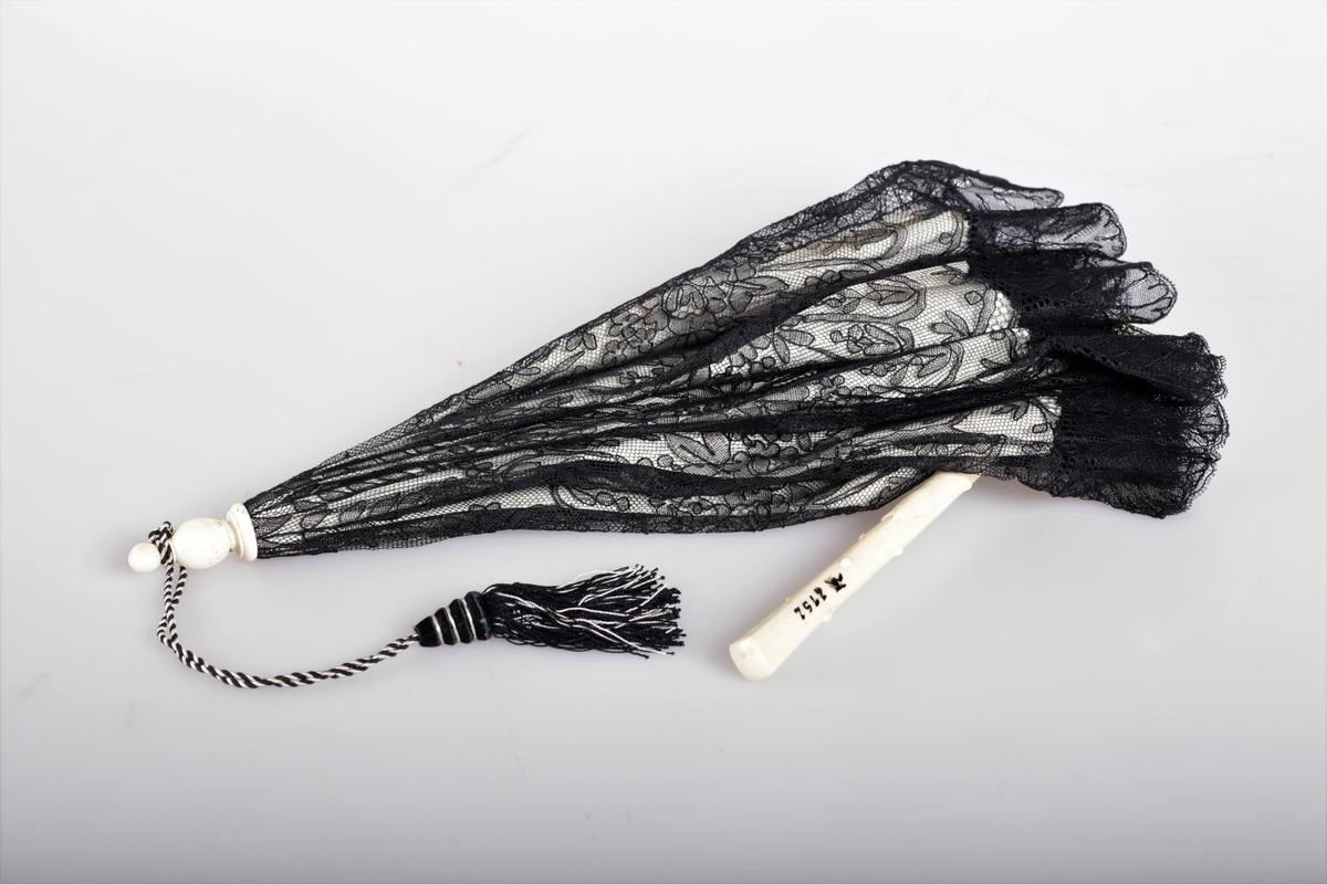 Parasoll av hvit silke og svart blonde over en stav av elfenben.