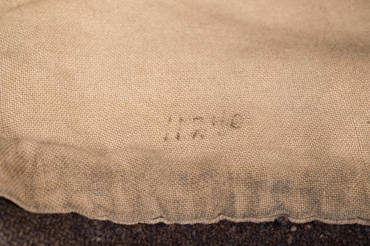 Mørkeblå fangelue i ull med naturhvitt for. På utsiden er en merkelapp med nummeret 16616 sydd på med sort tråd. På innsiden er numrene 8460 og 11240 påført med penn.