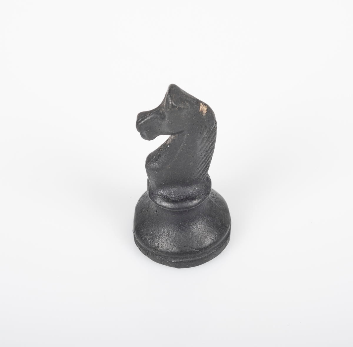 Sjakkbrikken (springer) er laget av tre, og er malt svart. Et lite avlangt hull på undersiden.