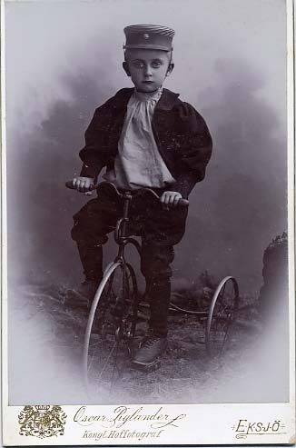 Kabinettsfotografi: gossen Rylander med keps på huvudet på en trehjulig barncykel.