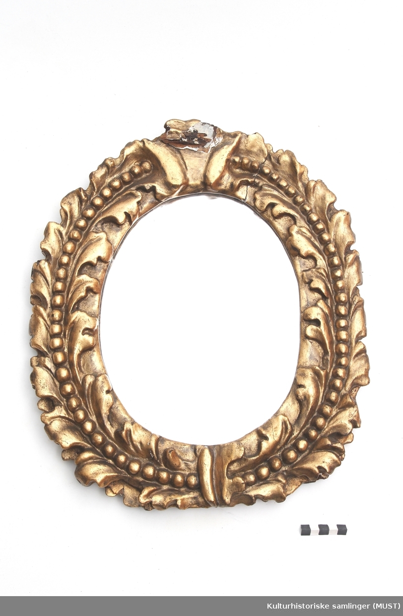 Ovalformet speil med med en enkel bladkrans rundt. I midten av denne går en perlerrad.