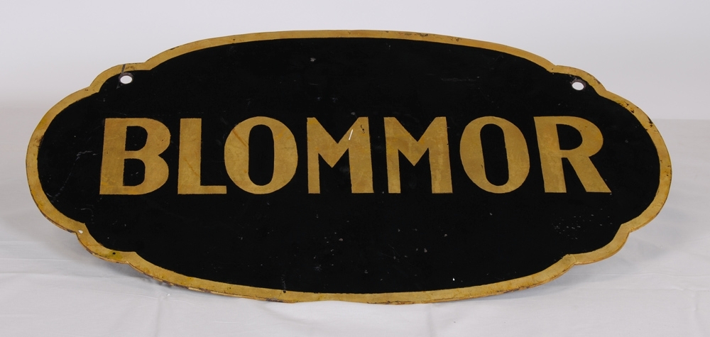 Dubbelsidig oval bemålad plåtskylt med en texten "BLOMMOR" på båda sidor i "guldfärg" mot svartmålad botten. Runt skylten är det en guldfärgad kant. Skylten är oval med fyra utbuktningar varav de två övre har hål för upphängning.

Se även Jvm 10423, 10425, 10426.