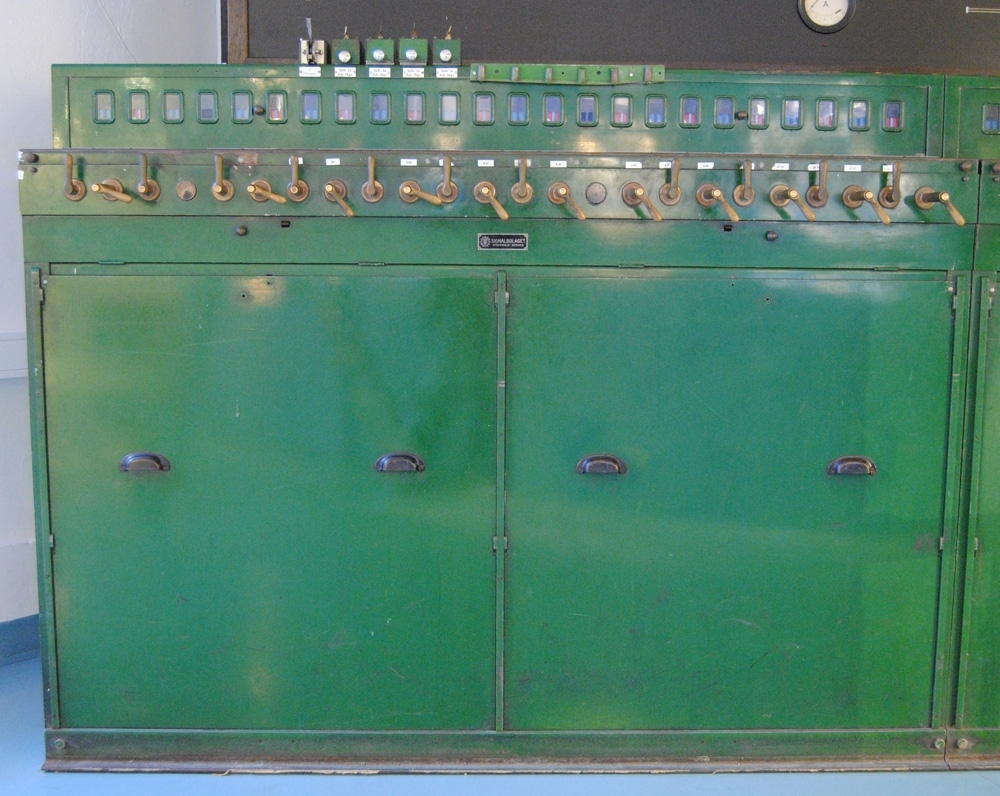 Elektriskt ställverk med elektriskt register. Enradigt ställverk. Grönt metallhölje. Består av två delar (Jvm 20212:1-2) med två luckor på framsidorna. Se Jvm 20212:3 för tillhörande spårplan. Längst upp till vänster sitter en grupp med knappar som fälles ut med en spärr. De är döpta Spår 1a-4a Avk. tågv. Dessutom finns en spak för "V3 Fällbommar". Ställverket har 24 stycken fönster på var del. Bakom dessa sitter blå och röda skyltar. På nästa etage sitter handtag, omväxlande små och stora, varav de stora har en tryckknapp som måste hållas inne då handtaget vrids åt vänster, men inte då det ska återställas. De stora handtagen är för växlar och spårspärr till växlar, och de små är för signaler. I mitten av en lucka på nedanför handtagen sitter en metallskylt "SIGNALBOLAGET STOCKHOLM SWEDEN". Luckan har två knoppar och går att öppna om två spärrar trycks in.