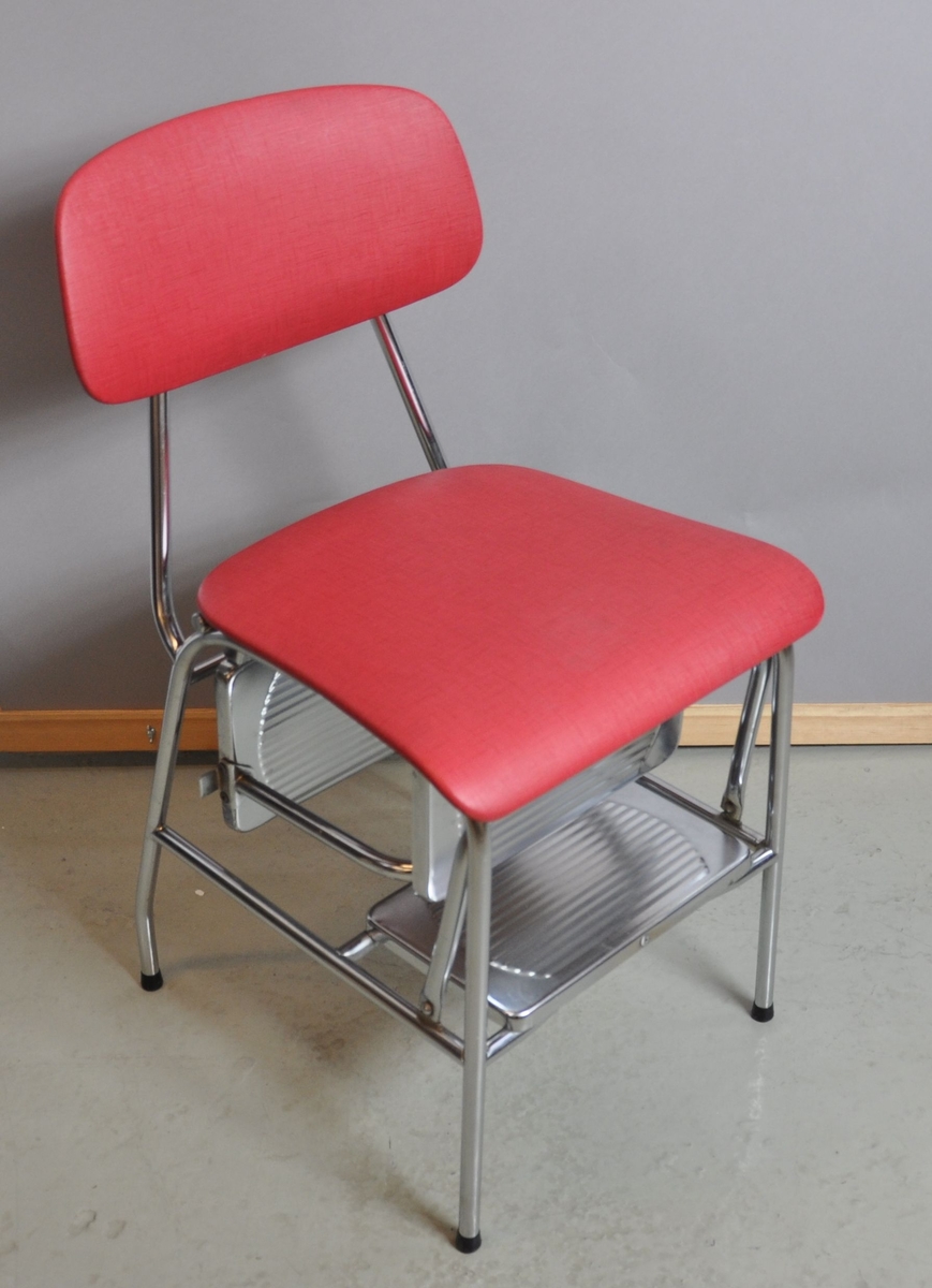 Husmorsstol. Stolen er laget av metall og trekt med rødt plastikksskinn. Setet kan løftes bakover slik at stolen fungerer som en trappestige med tre trinn.