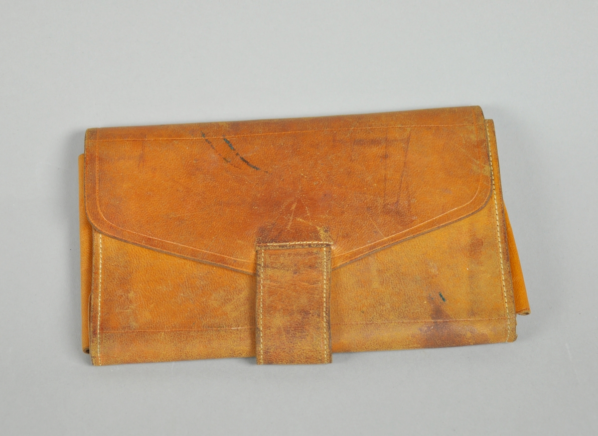 Lommebok av skinn med en lomme til sedler, og en lomme som kan lukkes til mynt. Lommeboken lukkes med en skinnreim som legges rundt gjenstanden og gjennom en skinnhempe.