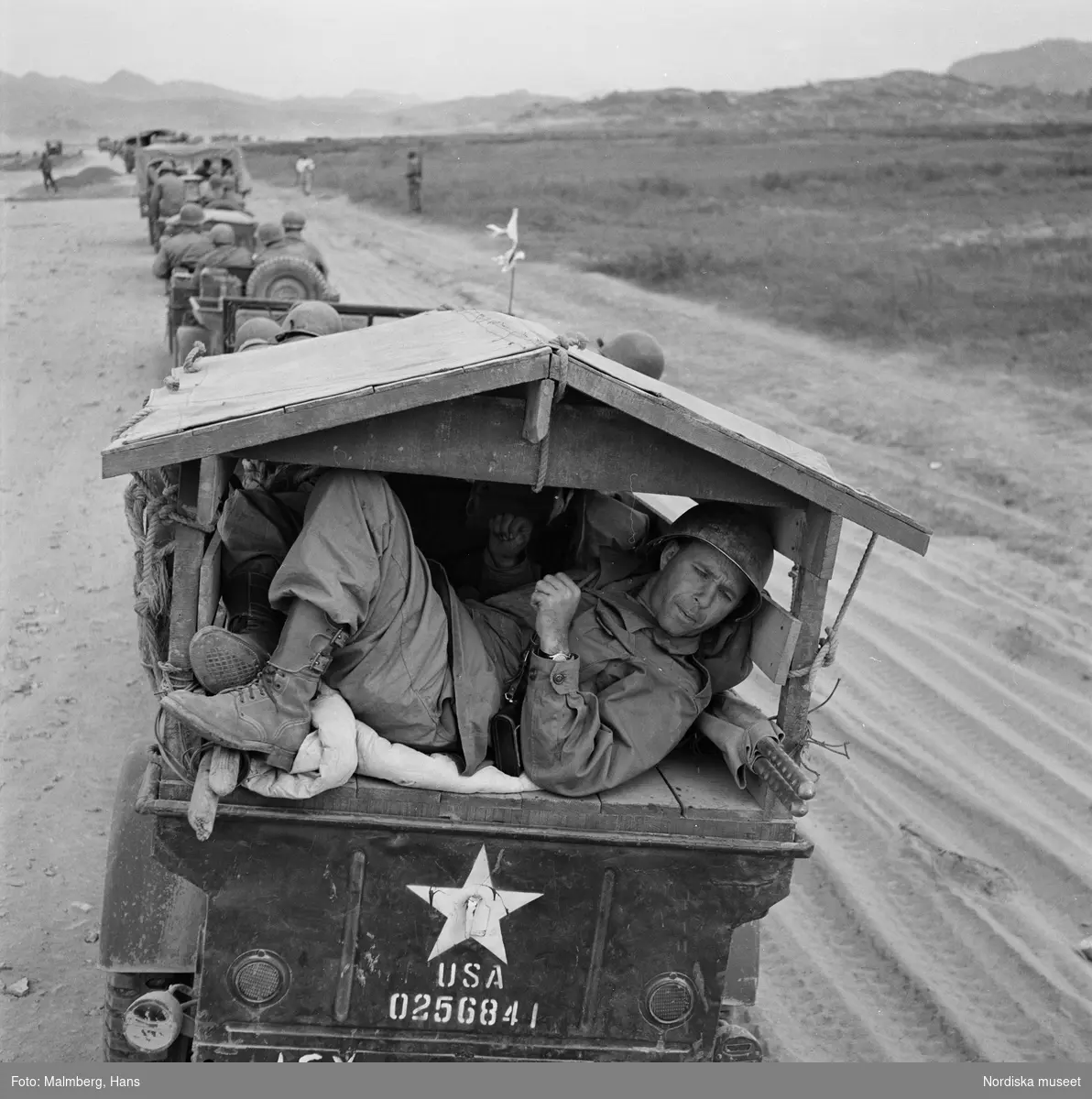 Koreakriget. En kolonn med amerikanska jeep-fordon på en väg. En amerikansk soldat ligger på en av bilarnas lastflak.