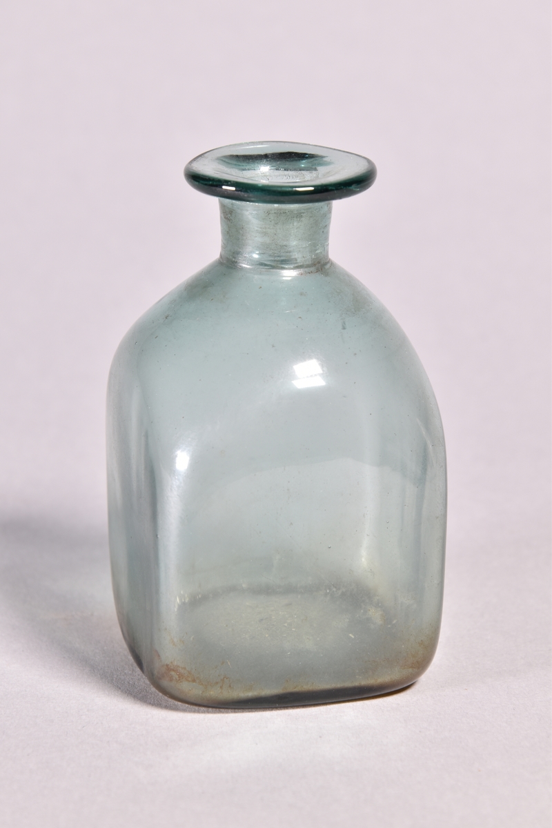 Flaska av grönt glas, kvadratisk med kort hals och utvikt mynning.