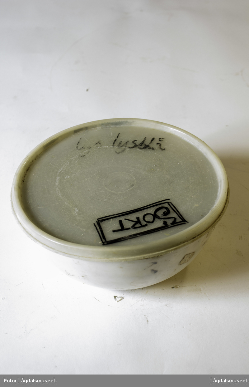 Plastbolle med lokk med uttørket pipeleire i fargen svart. Pipeleiren ble brukt til begitting av keramikken.