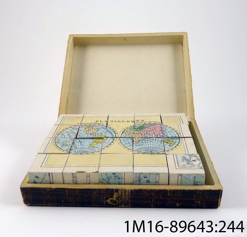 Pussel bestående av 20 vändbara kuber. Motivet är kartor på alla sidor. Kuberna förvaras i en pappask med guldkant.