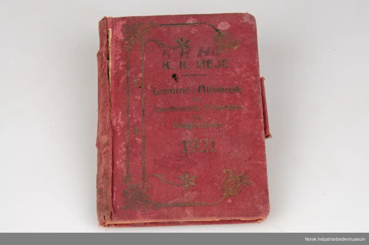 Liten rød notisbok og almanakk med harde bokrygger og en gang utsmykket med gullskrift. Serieprodusert publikasjon som sannsynligvis var i bruk fra 1921. Forholdsvis slitt rygg. Sidene 2 tom 4 er løsrevne fra bokryggen.